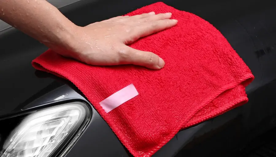 Une personne utilise une des astuces de grand mere pour nettoyer les phares de voiture avec un chiffon en micro-fibre