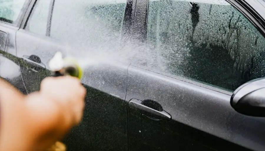 Une personne nettoie sa voiture avec un jet d'eau